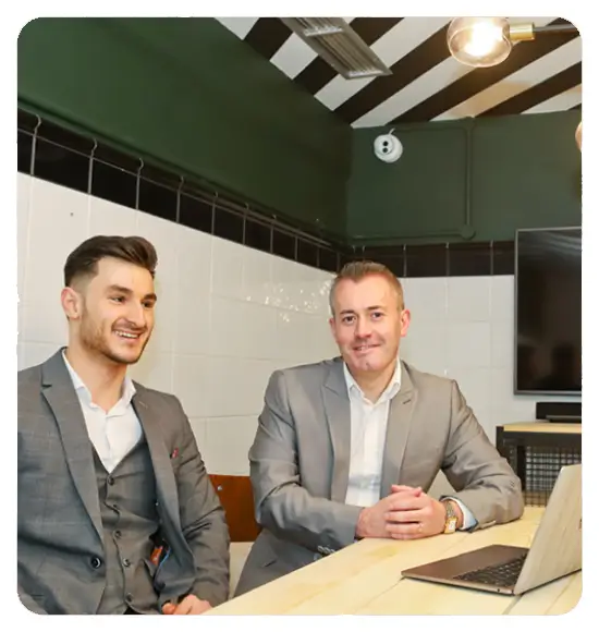Two financial advisers in Dorset seated at a table with a laptop, discussing financial strategies or services, representing a professional consultation in accounting or finance.