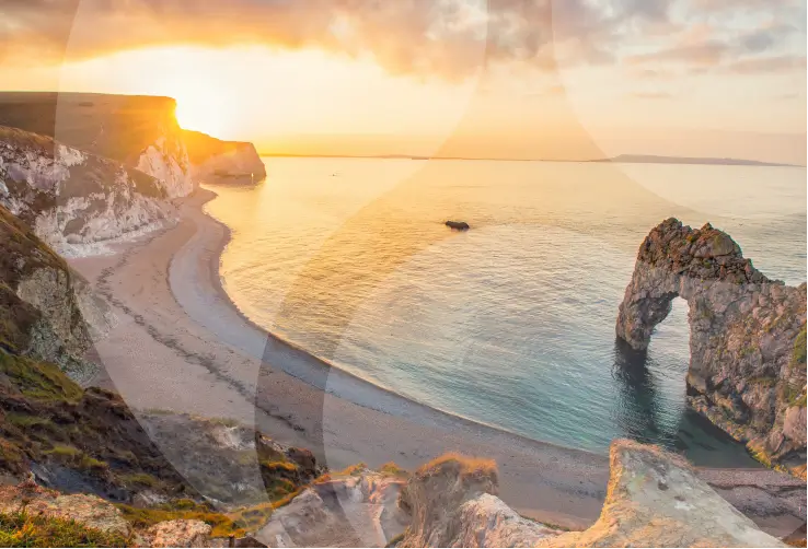 A breathtaking view of Durdle Door and the surrounding coastline at sunset, with the golden light reflecting off the calm sea, showcasing the natural beauty of the Dorset coast.