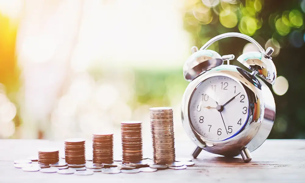An alarm clock sat next to piles of coins increasing in size to demonstrate a rising chart.
