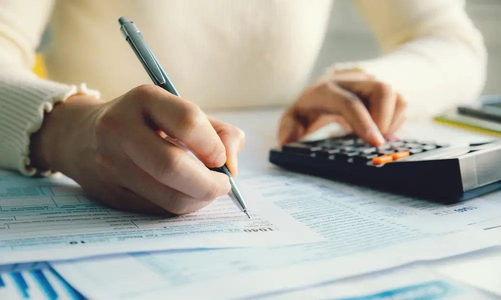 Business owner sitting down working out their accounts with tax documents and a calculator.
