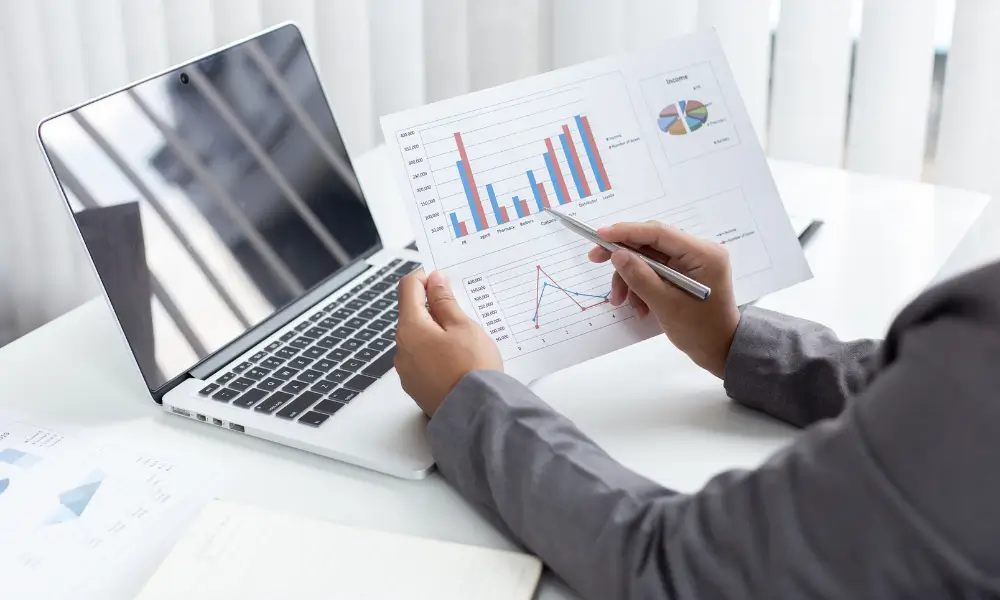 A business owner going over their accounts looking at charts on a piece of A4 paper in front of a laptop.