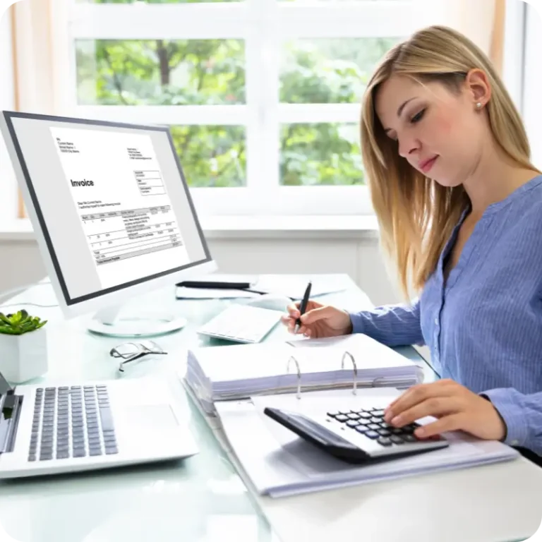 Accountant sitting at a desk, with a laptop, and calculator with a pc showing an invoice on the screen.