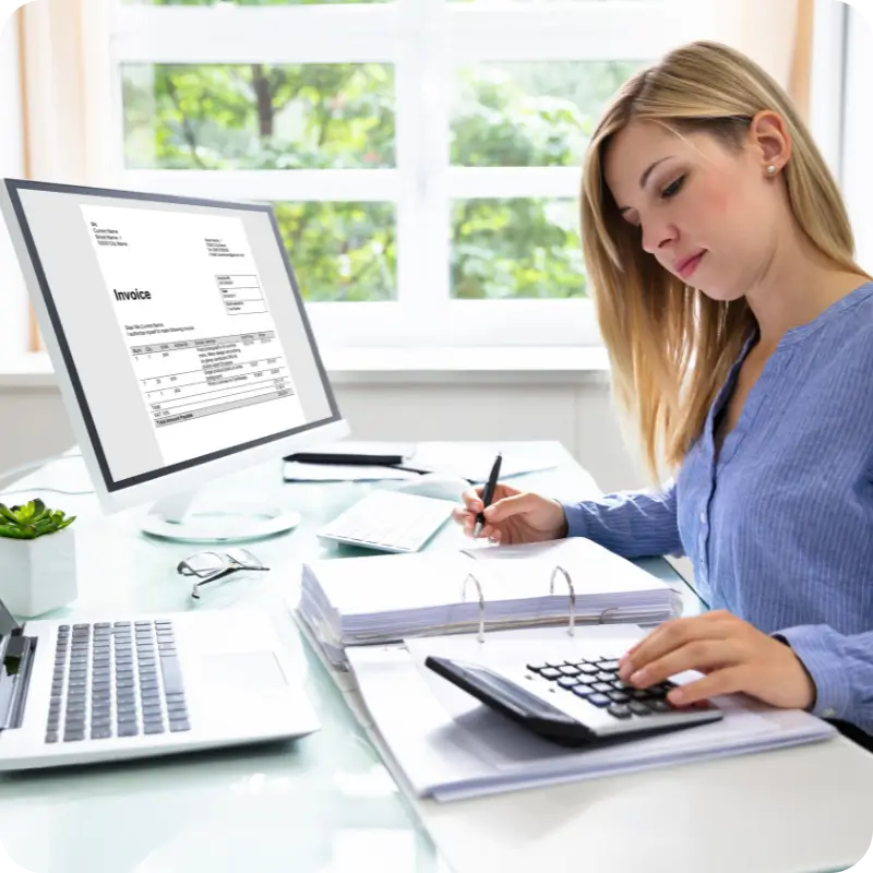 Accountant sitting at a desk, with a laptop, and calculator with a pc showing an invoice on the screen.