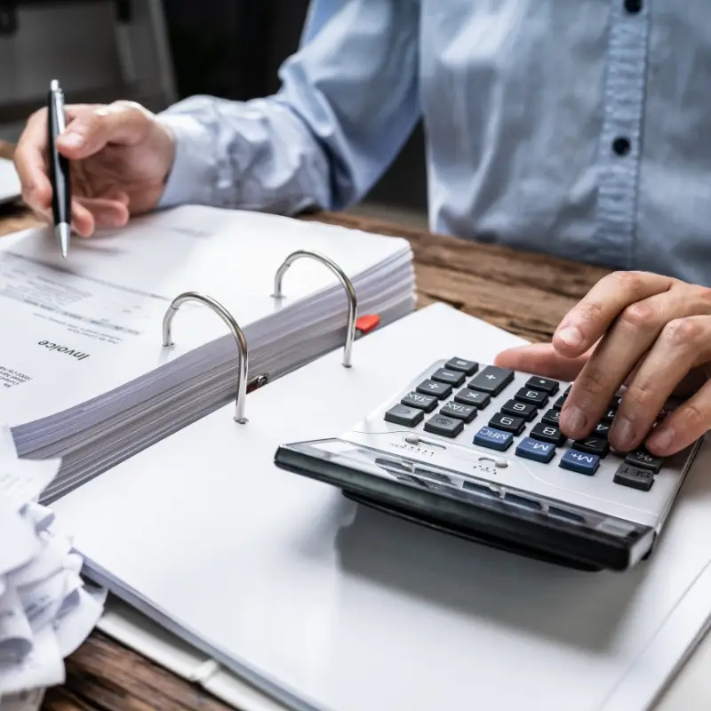 Personal tax accountant working at a desk punching in numbers into a calculator while looking at invoices.